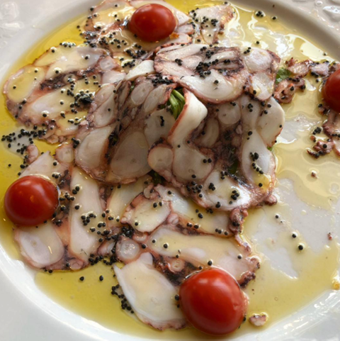 Oktopus-Carpaccio mit Olivenöl und Kirschtomaten auf weißem Teller